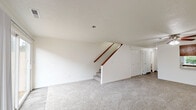 Located in Vancouver, Washington, this two-story, two-bedroom, three-bathroom home offers a practical and comfortable layout spread across two floors. The main level features an open living room with plush carpeting, a wood-burning fireplace framed by a clean white surround, and sliding glass doors that lead to an outdoor patio, filling the space with natural light. The kitchen is equipped with warm oak cabinetry, a full suite of white Whirlpool appliances including a refrigerator, electric range, and over-the-range microwave, complemented by wood-look tile flooring. A staircase with a wood handrail connects the two floors, and a ceiling fan overhead adds functionality to the living area. The upper level hosts both bedrooms, each carpeted and featuring vaulted ceilings and generous closet space—the primary bedroom includes dual sliding closet doors and a large window with outdoor views. A dedicated laundry area on the upper floor includes wood-look tile flooring, overhead oak cabinetry, and full washer and dryer hookups. The three bathrooms are finished with wood-look tile flooring, warm wood vanities, and clean white fixtures, with at least one bathroom featuring a glass-panel shower enclosure.