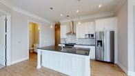 Located at 1414 Broadview Ave in Columbus, Ohio, this single-floor residence offers a thoughtfully designed layout with modern finishes and a clean, contemporary aesthetic. The heart of the home is a well-appointed kitchen that immediately draws attention with its expansive center island, topped with a sleek dark countertop that provides generous prep and seating space. Crisp white shaker-style cabinetry lines the walls, complemented by a classic marble-style tile backsplash that adds texture and elegance. A stainless steel range hood serves as a focal point above the range, while a full suite of stainless steel appliances — including a French door refrigerator with an in-door ice and water dispenser — ensures both style and functionality. Pendant lighting with glass globe fixtures hangs above the island, casting warm ambient light throughout the space. Light-toned hardwood flooring runs throughout, enhancing the bright and airy feel created by recessed ceiling lighting and crown molding details. Arched doorways provide graceful transitions between spaces. A glimpse into an adjacent bathroom reveals classic tile work, maintaining the home's consistent attention to detail and quality craftsmanship throughout.