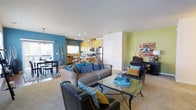 This two-floor residence offers a thoughtfully designed interior defined by bold color choices and an open, connected layout. The main living area makes an immediate impression with striking teal and yellow-green accent walls that lend the space a lively, contemporary character. Recessed lighting and a textured ceiling complement the bright, welcoming atmosphere throughout.

The living room is generously proportioned, centered around a glass-top coffee table and anchored by a plush sofa adorned with vibrant blue and neutral throw pillows. A leather accent chair adds a refined contrast, while a dedicated workspace area is neatly tucked to one side, maximizing the utility of the open floor plan.

The kitchen flows seamlessly from the living area and features light wood cabinetry, stainless steel appliances including a refrigerator and microwave, and a functional counter layout ideal for everyday cooking. An adjacent dining area benefits from natural light filtering in through a sliding glass door that opens to an outdoor balcony, extending the living space outdoors.

The open-concept design ensures a natural transition between the living, dining, and kitchen zones, making the home feel spacious and connected. With its vibrant palette, modern finishes, and practical layout spread across two floors, this residence delivers a dynamic and comfortable living experience.
