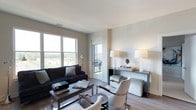 This well-appointed 2-bedroom, 2-bathroom residence offers a thoughtfully designed single-floor layout that balances comfort and contemporary style. The living area serves as the heart of the home, showcasing hardwood flooring, neutral wall tones, and large double-hung windows that flood the space with natural light and frame expansive outdoor views of the surrounding landscape. A sliding glass door provides direct access to a private balcony, seamlessly connecting indoor and outdoor living. The living room is elegantly furnished with a deep navy sofa, chrome-accented side chairs, and a sleek console table adorned with statement table lamps, creating a sophisticated yet inviting atmosphere. The clean architectural lines and recessed ceiling details contribute to a polished, modern aesthetic throughout. The overall ambiance is bright, airy, and refined, with a neutral palette that allows the quality of the finishes and the abundance of natural light to take center stage. With two well-proportioned bedrooms and two full bathrooms, this residence provides both functionality and style, making it an ideal space for those seeking modern urban living with a comfortable, upscale feel.