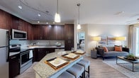 This well-appointed single-floor residence offers a thoughtfully designed open-concept layout that seamlessly connects the kitchen, dining, and living areas. The kitchen is a standout feature, showcasing rich dark-wood cabinetry, granite countertops, a tiled backsplash, stainless steel appliances — including a refrigerator, range, and built-in microwave — and a curved breakfast bar with seating for multiple guests. Pendant lights and a track lighting system illuminate the space with both style and functionality. Adjacent to the kitchen, a dedicated dining nook provides an intimate setting beneath a contemporary pendant light. The living room is bright and inviting, with light wood-style flooring, a ceiling fan, and a sliding glass door that opens to a private balcony with lush outdoor views. Both bedrooms are carpeted and bathed in natural light from large windows dressed with blinds and draping curtains. Each bedroom benefits from access to a well-finished bathroom featuring granite vanity countertops, dark cabinetry, and tile flooring. One bathroom includes a full soaking tub and shower combination. Neutral tones, clean architectural lines, and consistent high-quality finishes create a cohesive and comfortable ambiance throughout the entire residence.