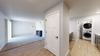This single-floor residence offers a thoughtfully updated interior with a clean, modern aesthetic throughout. Light-toned luxury vinyl plank flooring runs through the main living and kitchen areas, while plush carpet adds warmth to the bedrooms and closet spaces. The open entryway connects seamlessly to the living area, which features a freestanding fireplace and a wall-mounted HVAC unit, providing both comfort and character. Natural light filters into the carpeted bedrooms, each equipped with ceiling fans and baseboard heating; one bedroom includes a spacious walk-in closet with wire shelving for ample storage. The updated bathroom features wood-toned cabinetry, a white countertop, and contemporary black hardware under stylish vanity lighting. The galley-style kitchen is outfitted with stainless steel appliances, including a large French door refrigerator, dark cabinetry, and recessed lighting overhead. A notable feature is the in-unit stacked washer and dryer, conveniently located within the kitchen corridor. Craftsman-style interior doors with matte black hardware add a refined touch throughout. The neutral color palette and updated finishes create a cohesive, move-in-ready environment well-suited for modern living.