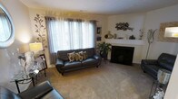 This three-floor home is thoughtfully designed to maximize functionality across its multiple levels, connected by a staircase finished with warm hardwood treads and a metal railing. The stairwell is clean and minimal, with crisp white walls and decorative accents that create an inviting transition between floors.

The living room is a comfortable, carpeted space centered around a fireplace with a white mantel, providing a natural focal point. Large windows dressed with layered curtains and blinds allow natural light to fill the room, enhancing the relaxed atmosphere. The neutral palette throughout creates a calm, cohesive environment.

The kitchen is well-appointed and efficient, featuring light maple cabinetry paired with dark granite-style countertops for a classic contrast. Stainless steel appliances, including a gas range and dishwasher, add a modern touch. A window above the sink brings in additional natural light, while a track lighting fixture overhead ensures the space remains bright. The hardwood-style flooring grounds the room and adds warmth. Together, the floors offer a well-rounded and functional living environment.