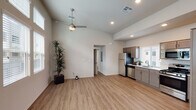 This well-appointed single-floor residence offers a thoughtfully designed open-concept layout that seamlessly connects the living and kitchen areas. The kitchen is a standout feature, outfitted with a full suite of stainless steel appliances including a refrigerator, gas range, over-the-range microwave, and dishwasher. Two-toned cabinetry in warm taupe and darker brown tones pairs with light countertops and a single-basin sink positioned beneath a window that fills the space with natural light. Wood-look luxury vinyl plank flooring extends throughout the main living areas, adding warmth and continuity.

The living area is generously proportioned with vaulted ceilings and a ceiling fan overhead, creating an airy, open ambiance. Neutral white walls provide a clean backdrop, and a doorway connects to the private rooms beyond. The bedroom features plush carpeting, a ceiling fan with light, a window with blinds, and a stylish sliding barn door that adds a modern rustic touch.

The bathroom is efficiently designed with wood-look flooring, a walk-in glass-enclosed shower, a toilet, and a single-sink vanity topped with a white countertop and framed by a large mirror. Windows throughout the unit invite natural light while maintaining privacy with slatted blinds. The overall aesthetic is clean, contemporary, and move-in ready.