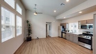 This well-appointed single-floor residence offers a thoughtfully designed open-concept layout that seamlessly connects the living and kitchen areas. The kitchen is a standout feature, outfitted with a full suite of stainless steel appliances including a refrigerator, gas range, over-the-range microwave, and dishwasher. Two-toned cabinetry in warm taupe and darker brown tones pairs with light countertops and a single-basin sink positioned beneath a window that fills the space with natural light. Wood-look luxury vinyl plank flooring extends throughout the main living areas, adding warmth and continuity.

The living area is generously proportioned with vaulted ceilings and a ceiling fan overhead, creating an airy, open ambiance. Neutral white walls provide a clean backdrop, and a doorway connects to the private rooms beyond. The bedroom features plush carpeting, a ceiling fan with light, a window with blinds, and a stylish sliding barn door that adds a modern rustic touch.

The bathroom is efficiently designed with wood-look flooring, a walk-in glass-enclosed shower, a toilet, and a single-sink vanity topped with a white countertop and framed by a large mirror. Windows throughout the unit invite natural light while maintaining privacy with slatted blinds. The overall aesthetic is clean, contemporary, and move-in ready.