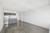 Located at 756 Garland Ave in the heart of Los Angeles, this compact studio unit offers a well-organized single-floor layout comprising a living area and a full bathroom. The living space features polished concrete floors that lend an industrial-modern aesthetic, complemented by clean white walls and a textured ceiling. A large window floods the room with natural light while offering views of the surrounding Los Angeles cityscape, and a wall-mounted HVAC unit ensures year-round climate control. A built-in kitchenette along one wall provides gray cabinetry, open shelving, a sink, and a compact refrigerator, making efficient use of the available space. An open closet with a hanging rod is integrated into the living area, offering convenient storage. The bathroom is cleanly finished with a gray vanity, white countertop, a large mirror with overhead lighting, and mosaic tile flooring, presenting a modern and functional design. The overall ambiance of the unit is minimalist and bright, with a neutral color palette throughout that creates a versatile canvas well-suited to urban living in one of Los Angeles's central neighborhoods.