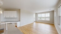 This single-floor residence is designed with a clean, contemporary aesthetic that emphasizes openness and functionality. The open-concept living and dining area flows seamlessly from the kitchen, unified by warm hardwood-style flooring that extends throughout the main living spaces. Large windows fitted with horizontal blinds invite abundant natural light and offer outdoor views, enhancing the airy ambiance of the space.

The kitchen serves as a central focal point, featuring a substantial island with a dark countertop, crisp white shaker-style cabinetry extending to the ceiling, a white subway tile backsplash, and a full suite of stainless steel appliances including a gas range, over-the-range microwave, and French door refrigerator. Pendant lighting with glass globe fixtures adds a stylish touch above the island.

A dedicated bedroom area benefits from multiple windows on two walls, filling the room with natural light and providing expansive outdoor views. The bathroom is finished with large-format tile flooring, a dark-toned vanity with a white countertop, a framed mirror with overhead lighting, and a tub-shower combination. A dedicated laundry area houses a full-size top-loading washer and dryer with overhead wire shelving for added storage.