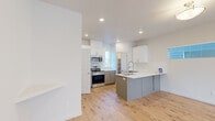 This well-appointed multi-story home spans three floors and offers four bedrooms and four bathrooms, thoughtfully laid out to maximize both function and comfort. The main living level showcases an open-concept kitchen and living room anchored by a central island with a sleek gray base, white quartz countertops, and a dual-basin sink with a pull-down faucet. White upper cabinetry pairs with gray lower cabinets, while stainless steel appliances—including a range and over-the-range microwave—add a modern touch. Light hardwood flooring runs throughout the main level, complementing the crisp white walls and recessed lighting. A dedicated walk-in pantry with built-in shelving provides ample storage. Hallways connect the floors via carpeted staircases with clean white trim, transitioning seamlessly between levels. The bedrooms feature plush carpet flooring, neutral white walls, and windows that allow natural light to fill each room. The primary bedroom offers a generous footprint. The bathrooms are finished with gray vanity cabinetry, white countertops, large mirrors, hardwood-style flooring, and glass-enclosed showers. Throughout the home, the consistent use of neutral tones, modern fixtures, and quality finishes creates a clean, contemporary aesthetic.
