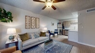 This single-floor residence offers a thoughtfully designed open-concept layout that seamlessly connects the living, dining, and kitchen areas. The living room is a welcoming space featuring light wood-look flooring, a textured ceiling, and a ceiling fan overhead. Large windows dressed with sheer curtains allow natural light to fill the room, creating a bright and airy atmosphere. Decorative wall art and a mix of contemporary furnishings — including a tufted sofa, leather accent chair, and a glass coffee table — lend the space a modern yet comfortable character. The dining nook sits adjacent to the living area, offering a natural transition into the kitchen. The kitchen is well-equipped with warm wood-toned cabinetry, white quartz countertops, a subway tile-style backsplash, stainless steel appliances including a dishwasher and refrigerator, and in-unit washer and dryer. A kitchen island provides additional counter space and a casual dining option. Both bedrooms feature ceiling fans, light wood-look flooring, and windows with blinds for privacy and light control. Each room is comfortably sized and designed for rest and relaxation. The bathroom is clean and functional, complete with a shower-tub combination, wood-toned vanity, and white countertop. Throughout the residence, a cohesive neutral color palette with warm accents creates a consistent and inviting aesthetic.