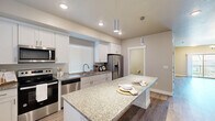 This two-story home offers 3 bedrooms and 2 bathrooms thoughtfully distributed across two well-proportioned floors. The main level features an open-concept kitchen and living area anchored by light hardwood-style flooring throughout. The kitchen is a standout, boasting white shaker cabinetry, granite countertops, a large central island with pendant lighting, and a full suite of stainless steel appliances including a range, dishwasher, microwave, and French door refrigerator. Natural light fills the space through multiple windows dressed with clean white blinds. The living room is spacious and airy, highlighted by a classic chandelier and a ceiling fan, with a sliding glass door that invites additional light. A staircase connects to the upper floor, where the bedrooms are located. The primary bedroom is a comfortable size, and the bathrooms are well-appointed — the full bath features a wide dual-sink vanity with white cabinetry, a large mirror, wood-look flooring, and a glass-enclosed shower. The bedrooms are carpeted and include double-door closets for ample storage. Neutral warm-toned walls throughout create a cohesive, move-in-ready aesthetic that suits a variety of styles.