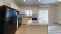 This two-story residence is designed with a clean, modern aesthetic throughout. The kitchen serves as a functional centerpiece, featuring white shaker-style cabinetry, granite countertops, and light hardwood-style flooring. Black appliances—including a refrigerator, electric range, built-in microwave, and dishwasher—provide a sharp contrast against the bright cabinetry. A central island with additional granite surface space enhances both prep area and visual appeal, while a window above the sink allows natural light to fill the space.

The bedrooms are finished with plush wall-to-wall carpeting and feature windows fitted with blinds for light control. One bedroom includes a generously sized walk-in closet equipped with dual hanging rods and built-in shelving. Ceiling heights in the upper level appear notably tall, adding an open, airy quality to the living areas.

The bathrooms are consistently finished with granite-topped white vanities, tile flooring, and full shower-tub combinations with built-in shelving. Recessed lighting provides clean, even illumination throughout.

The attached garage offers a spacious, enclosed area with a concrete floor and an automatic opener, providing convenient and secure vehicle storage.