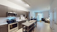 This contemporary single-floor residence offers a thoughtfully designed open-concept layout that seamlessly connects the kitchen, dining, and living areas. The kitchen is a standout feature, outfitted with dark wood cabinetry, granite countertops, stainless steel appliances including a refrigerator, range, microwave, and dishwasher, a tile backsplash, and a central island with additional storage. Light wood-style flooring runs throughout the main living areas, complementing the clean, neutral palette.

The living and dining space benefits from large floor-to-ceiling windows with vertical blinds, allowing abundant natural light to fill the room. Track lighting in the kitchen and pendant fixtures in the dining area add to the modern aesthetic.

The primary bedroom features a distinctive wood panel accent wall serving as a headboard backdrop, while the secondary bedroom offers a bright, airy feel with a large window and light wood floors. Both bedrooms provide a calm, restful atmosphere.

The primary bathroom includes a dual-sink vanity with dark wood cabinetry, a white quartz countertop, and a glass-enclosed shower. The secondary bathroom features a single vanity with matching cabinetry and a shower-tub combination. A generously sized walk-in closet with wire shelving offers ample storage throughout.