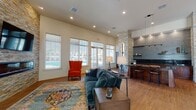 Located at 1194 Blue Ridge Ave in Crozet, Virginia, this single-floor community clubhouse offers a thoughtfully designed and well-appointed gathering space. The open-concept lounge area serves as the heart of the facility, anchored by a striking stacked-stone accent wall that houses a linear electric fireplace and a wall-mounted television. Warm hardwood flooring, recessed lighting, and large windows flooding the space with natural light create an inviting atmosphere. Views of the outdoor pool area can be enjoyed directly from the lounge seating.

The kitchenette and bar area is finished with rich wood cabinetry, dark granite countertops, a glass tile backsplash, floating wood shelves, and a built-in beverage refrigerator — providing an ideal space for socializing and entertaining. A granite-topped bar with seating completes this area.

The fitness center is generously sized and fully equipped with a variety of cardio machines, including ellipticals and stair climbers, as well as cable and resistance machines. Floor-to-ceiling mirrors, overhead lighting, and ceiling fans keep the space bright and comfortable. Adjacent to the gym is a dedicated studio or yoga room featuring hardwood floors, mirrored walls, a wall-mounted display screen, and high ceilings, ideal for group fitness or individual training sessions.