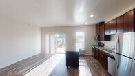 Located at 3745 Technology Dr NW in Rochester, Minnesota, this single-floor unit offers a well-designed, open-concept layout that seamlessly connects the kitchen and living areas. The kitchen is a standout feature, equipped with rich dark-wood cabinetry extending to the ceiling, granite countertops, and a full suite of stainless steel appliances including a refrigerator, range, microwave, and dishwasher. A center island with a matching granite surface provides additional prep space and a natural focal point for the room. Hardwood-style flooring runs throughout the main living areas, adding warmth and continuity to the space. The living area is bright and open, benefiting from natural light that streams in through a sliding glass door leading to an outdoor view, as well as additional windows. Recessed lighting and clean white walls enhance the airy, modern ambiance. An in-unit washer and dryer area is conveniently accessible off the kitchen. The bathroom features a granite-topped vanity with dark cabinetry consistent with the kitchen, a full tub and shower combination, and light-toned flooring that keeps the space feeling clean and functional. Overall, the unit presents a modern, cohesive design with practical amenities throughout.