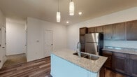 Located on Evergreen Street in Gardner, Kansas, this single-floor residence offers a thoughtfully designed layout with modern finishes and a welcoming ambiance. The open-concept kitchen serves as the heart of the home, showcasing rich dark-stained cabinetry, granite countertops, and a suite of stainless steel appliances including a refrigerator, electric range, and microwave. A central island with a double undermount sink and elegant pendant lighting above adds both functionality and style, while durable wood-look flooring ties the space together seamlessly.

The living area extends naturally from the kitchen, bathed in natural light from glass French doors that open to the outdoors, and is complemented by a ceiling fan overhead. The bedrooms are carpeted for comfort, each featuring ceiling fans and windows with blinds that allow for ample natural light and privacy.

The bathrooms are finished with wood-look flooring, clean white walls, and dark wood vanities topped with light countertops, offering a cohesive and polished aesthetic. One bathroom features a shower-tub combination, while another includes a walk-in shower setup. Throughout the home, neutral tones and quality materials create a clean, modern atmosphere suited for comfortable everyday living.