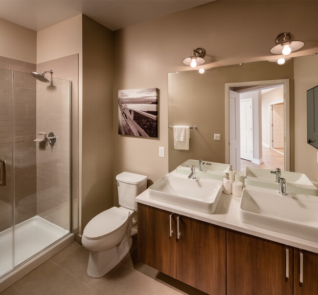 Baño de la colección Signature con gabinetes de roble, encimeras de cuarzo gris claro, protector contra salpicaduras de azulejos blancos y pisos de baldosas. - Avalon Princeton