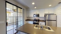 Located at 986 Westcreek Ln in Thousand Oaks, California, this single-floor residence offers a well-designed layout that balances functionality with comfort. The open-concept kitchen is a standout feature, outfitted with stainless steel appliances including a gas range, over-the-range microwave, and refrigerator. White shaker-style cabinetry lines the walls, complemented by dark countertops and a peninsula with an integrated sink — ideal for both meal preparation and casual dining. Rich, dark hardwood flooring extends through the kitchen and living areas, adding warmth and contrast to the neutral color palette. The living area benefits from abundant natural light through large windows with grid-style sliding glass doors that open to an outdoor space, and a ceiling fan adds comfort overhead. The bedrooms are carpeted and feature mirrored sliding closet doors, providing generous storage. The primary suite includes an elongated en-suite bathroom with a dual-sink vanity, dark countertops, white cabinetry, and a separate water closet. A secondary bathroom mirrors the same clean, modern aesthetic with a single-sink vanity and dark hardwood flooring. Throughout, the space maintains a cohesive, contemporary design with neutral tones, recessed lighting, and crisp white trim.