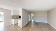 This single-story space is designed with a functional, open layout that connects the main living area to the kitchen, creating a seamless flow throughout. The living space features wood-look laminate flooring and neutral gray walls, complemented by a textured ceiling that extends across the common areas.

The kitchen is efficiently arranged with white shaker-style cabinetry, a stone tile backsplash, and light-toned countertops. Stainless steel appliances include a gas range, over-the-range microwave, and refrigerator, providing a well-equipped cooking space. A peninsula with an integrated sink separates the kitchen from the living area.

The bedrooms are finished with plush carpeting and neutral walls, offering a comfortable setting. One bedroom includes a ceiling fan with a built-in light fixture and a window with vertical blinds, allowing natural light to enter. The additional bedroom provides a similarly calm, well-proportioned space.

The bathroom includes a white soaking tub and shower combination, a single-sink vanity with a light stone countertop, wood-look flooring, and chrome fixtures. A wall-mounted grab bar adds a practical detail. Overall, the space maintains a clean, move-in-ready aesthetic with consistent neutral finishes throughout.