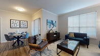 This single-story, one-bedroom, one-bathroom residence offers a thoughtfully designed layout that maximizes comfort and functionality. The open living area features rich hardwood-style flooring, elegant crown molding, and large windows with blinds that invite generous natural light. The living room provides ample space for seating and flows seamlessly into a dedicated dining area, which includes a sliding glass door with vertical blinds offering additional light and access.

The kitchen is equipped with dark cabinetry, black appliances including a refrigerator, electric range, and dishwasher, complemented by a gray subway tile backsplash and light countertops. An adjacent utility closet houses in-unit laundry connections.

The bedroom is carpeted for warmth and comfort, featuring a bright window with blinds, a ceiling fan, and sufficient space for a full furniture arrangement. The bathroom includes a single vanity with speckled countertops, a large mirror, and brushed nickel fixtures.

Throughout the residence, neutral gray walls provide a versatile backdrop, while crown molding in the main living areas adds a refined architectural detail. The cohesive design and practical layout make this a well-rounded and inviting single-floor home.