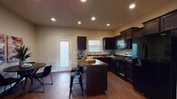 This two-story space is designed with a cohesive aesthetic that balances functionality and comfort throughout. The kitchen serves as a central highlight on the main floor, showcasing rich dark espresso cabinetry that extends to the ceiling, complemented by granite-look countertops and a matching central island with bar seating. Black appliances, including a range, microwave, refrigerator, and dishwasher, complete the kitchen suite. Recessed lighting illuminates the space, while a door with a frosted glass panel provides additional natural light and exterior access. An adjoining dining area adds convenience for everyday living.

The main level also features a living area with wood-look flooring, a ceiling fan, and large windows fitted with blinds that allow for ample natural light. A half bathroom on this floor includes wood-look flooring and neutral warm-toned walls.

Upstairs, a carpeted hallway with a white-railed balustrade connects the bedrooms. The bedrooms are comfortable in scale, each featuring plush carpet, ceiling fans with lighting, and windows that bring in natural light. The upper level also includes bathroom facilities, maintaining the same neutral warm palette found throughout the space.