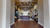 This single-floor community clubhouse at Turnberry Place offers a thoughtfully designed gathering space that blends elegance with practical amenities. The centerpiece is a grand lounge area distinguished by soaring coffered ceilings, dual ceiling fans, and rich wood-look tile flooring that flows throughout the entire facility. A dramatic stone-accented fireplace with a mounted TV anchors one end of the lounge, while columned archways and a wall of French doors bathe the space in natural light and provide views of the outdoor patio area.

A dedicated seating nook near expansive windows offers an inviting retreat filled with natural light, perfect for relaxed conversation. The business center is equipped with built-in workstations, bar-height seating, a printer, a curated bookshelf, and a wall-mounted TV for resident convenience. Adjacent to the main lounge, glass-enclosed leasing offices provide a professional yet welcoming environment.

The kitchenette features dark cabinetry, granite-look countertops, stainless steel appliances, and a water filtration station. The well-equipped fitness center includes cardio machines, a multi-station strength system, rubber flooring, ceiling fans, and abundant window light. A private tanning room rounds out the suite of amenities, completing this comprehensive and stylishly appointed community hub.