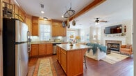 This thoughtfully designed single-floor home offers a seamless open-concept layout that connects the kitchen, dining area, and living room into one cohesive and inviting space. The kitchen is a standout, featuring warm honey-toned wood cabinetry, granite countertops, a central island with bar seating, a hanging pot rack suspended from an exposed wood beam, and a full suite of stainless steel appliances. Hardwood flooring flows throughout the main living areas, adding warmth and continuity.

The living room is anchored by a classic brick fireplace with a white painted mantle, crown molding, and a ceiling fan overhead. Natural light pours in through multiple windows fitted with horizontal blinds, creating a bright and airy atmosphere throughout. The dining area benefits from corner windows that frame views of the surrounding greenery.

The bedroom offers plush carpeting, crown molding, a ceiling fan, and access to a walk-in closet, providing a comfortable and functional retreat. The bathroom continues the consistent design language with wood cabinetry, granite countertops, tile flooring, and a well-lit vanity mirror. Throughout the home, the interplay of warm wood tones, neutral walls, and abundant natural light creates a welcoming and cohesive living environment.