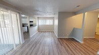 This well-appointed 3-bedroom, 2-bathroom single-story home offers a generous and thoughtfully designed floor plan. The open living and dining area is highlighted by light-toned wood-look flooring that flows throughout the space, neutral gray walls, and a textured ceiling. Large vertical-blind windows allow natural light to fill the room, creating a bright and welcoming atmosphere.

The kitchen is functionally designed with crisp white cabinetry, dark countertops, a tile backsplash, and a full suite of black appliances including a refrigerator, range, dishwasher, and over-range microwave. Track lighting and a window above the sink add both practicality and brightness to the space.

Each bedroom features the same wood-look flooring, neutral walls, and a textured ceiling. The primary bedroom includes direct access to a private en-suite bathroom, while a second full bathroom serves the remaining bedrooms. Both bathrooms are finished with large-format beige tile surrounding the tub-shower combinations, white vanities with updated fixtures, and wood-look flooring.

The layout, visible in the dollhouse view, is efficiently organized with well-proportioned rooms and clear sightlines, making the home feel open and connected throughout its single floor.