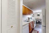 Located at 35700 E Michigan Ave in Wayne, Michigan, this one-bedroom, one-bathroom unit offers a practical and well-organized layout across a single floor. The galley-style kitchen is efficiently designed, featuring warm wood cabinetry, white appliances including a coil-top range, dishwasher, and refrigerator, as well as a single-basin sink and a ventilation hood. Wood-look flooring runs through the kitchen, which opens toward a dedicated dining area illuminated by a pendant light fixture. A textured ceiling adds a classic touch throughout the space. The living room is generously proportioned, featuring plush wall-to-wall carpeting and a large window that allows natural light to fill the room, creating a bright and inviting atmosphere. The bedroom offers comfortable proportions with soft carpeting underfoot, a natural light source via a street-facing window with curtains, and a louvered closet for convenient storage. The bathroom includes a vanity with an undermount sink, warm wood cabinetry, a wide mirror, and additional storage via a louvered closet in the adjacent hallway. Throughout the unit, neutral tones and clean lines contribute to a calm, functional ambiance well-suited for everyday living.