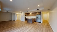 This contemporary single-floor unit showcases a clean, modern design highlighted by light hardwood flooring that runs consistently throughout every room, creating a cohesive and airy atmosphere. The open-concept layout connects the living area directly to the kitchen, maximizing the sense of space and encouraging easy flow between areas. The kitchen is a standout feature, outfitted with floor-to-ceiling wood-grain cabinetry, sleek white countertops, and a full suite of stainless steel appliances including a gas range, built-in microwave, dishwasher, and a French door refrigerator with an in-door water and ice dispenser. A centrally positioned kitchen island provides additional workspace and casual dining potential. Recessed lighting illuminates the kitchen and living spaces with a warm, even glow. The bedrooms are generously proportioned with clean white walls, recessed ceilings, and ample natural light. The bathrooms continue the modern aesthetic, featuring light wood-style flooring, a tub-shower combination with sliding glass doors and white tile surround, and clean chrome fixtures. Additional details include a dedicated closet space and efficient HVAC venting throughout, reflecting a thoughtfully designed and move-in-ready unit.
