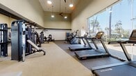 This well-appointed fitness center spans 890 square feet on a single floor, offering a wealth of exercise options in a bright, airy environment. The space boasts soaring ceilings with recessed lighting and ceiling fans, creating a sense of openness and comfort. Large windows allow natural light to flood the area, providing an invigorating atmosphere for workouts.

The facility is divided into distinct zones for various exercise types. The cardio section features multiple treadmills, elliptical machines, and stationary bikes, all equipped with digital displays. A dedicated strength training area includes a range of weight machines and free weights, catering to diverse fitness routines. The layout ensures ample space between equipment for safety and comfort.

The center's flooring is a combination of durable carpeting and rubberized surfaces, ideal for absorbing impact and reducing noise. Wall-mounted TVs and a sound system offer entertainment options during workouts. Additional amenities include a water station, towel service, and strategically placed mirrors for form checking.

Storage solutions for personal items and exercise accessories are provided, including weight racks and a rack for medicine balls. The overall design emphasizes functionality and user comfort, making it an inviting space for fitness enthusiasts of all levels.
