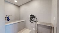 Located at 7395 E Legacy Blvd in Scottsdale, Arizona, this purpose-built pet spa offers a clean, modern environment designed with both pets and their owners in mind. The space is organized into two distinct areas accessible via a glass-paned door with a stainless steel threshold.

The reception and waiting area greets visitors with large-format tile flooring in a warm neutral palette, recessed lighting, and a set of French doors that invite natural light and views of the surrounding landscape. A warm wood credenza and a cushioned rocking chair provide a comfortable, relaxed atmosphere, while a posted Pet Spa Rules sign keeps guests informed.

Through the glass door lies the grooming room, finished in floor-to-ceiling grey subway tile for easy maintenance. The space features dual wash stations, each equipped with coiled hose attachments and framed by elegant marble-topped ledges. A textured penny-tile floor provides slip resistance throughout the wet zone. A wall-mounted professional pet dryer adds to the suite of grooming amenities. Recessed lighting illuminates the workspace evenly, and a stainless steel utility table offers additional prep surface. Together, the two rooms form a cohesive, well-appointed pet spa that balances functionality with a refined, contemporary aesthetic.