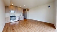 Located on the 6th floor at 532 Union St, Unit 610 in Oakland, CA, this 450-square-foot studio offers a well-designed, single-level open floor plan. The main living area is bright and airy, featuring warm-toned hardwood flooring throughout and crisp white walls that reflect natural light. A dramatic floor-to-ceiling sliding glass door dominates one wall of the living space, offering panoramic views of the Oakland cityscape, elevated freeways, and the distant bay and port—a striking visual feature of the unit. Recessed lighting provides consistent illumination across the space. The integrated kitchen is efficiently designed, featuring wood-toned cabinetry, a stainless steel gas range, microwave, dishwasher, and a clean white countertop with an undermount sink. Additional open shelving and a tall storage unit provide functional organization. A separate alcove area with hardwood flooring offers flexible use as a sleeping or workspace. The full bathroom is finished in a clean, modern style with neutral tile flooring, a soaking tub with a tiled shower surround, a wall-mounted vanity with an undermount sink, and a large mirror with built-in storage. The unit's contemporary finishes, efficient layout, and elevated city views make it a compelling urban residence.