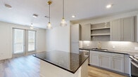 Located in Lewisville, TX, this thoughtfully designed one-bedroom, two-bathroom residence offers a cohesive blend of modern aesthetics and practical functionality across a single floor. The open-concept kitchen serves as the centerpiece of the living area, showcasing a substantial dark granite island beneath a pair of elegant ribbed glass pendant lights with gold brass hardware. Gray shaker-style cabinetry lines the walls alongside a subway tile backsplash, while stainless steel appliances — including a French door refrigerator, range, microwave, and dishwasher — provide a polished, contemporary finish. Gold-tone fixtures at the sink add a refined accent throughout. Durable wood-look flooring flows through the main living and kitchen areas, creating a warm and cohesive feel. The bedroom is a comfortable, well-proportioned retreat finished with plush carpet, a ceiling fan, and a window offering natural light and outdoor views. The primary bathroom features wood-look flooring, a granite-topped vanity with gold accents, and a tub/shower combination dressed in large-format marble-style tile with gold fixtures. A dedicated walk-in closet provides generous storage. The second bathroom mirrors the same upscale design language, ensuring consistency throughout the residence.