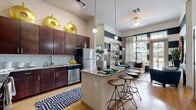 Located in the Baldwin Park neighborhood of Orlando, Florida, this single-floor residence delivers a thoughtfully designed interior with a contemporary aesthetic throughout. The open-concept kitchen is outfitted with rich dark wood cabinetry, granite countertops, a white subway tile backsplash, and stainless steel appliances. A curved kitchen island with pendant lighting and bar seating connects seamlessly to the main living area, making it ideal for entertaining. The living room commands attention with soaring ceilings, bold navy and white horizontal striped walls, and oversized grid-pane windows paired with a glass door that flood the space with natural light and offer views of the lush outdoor surroundings. A dedicated study features large windows with garden views, built-in shelving, and a versatile layout suited for a home office. The bedroom is an elegantly appointed retreat with soft sage-green walls, plush carpeting, and ample natural light. A generously sized walk-in closet with built-in shelving and wood-look flooring provides excellent storage. The bathroom is finished with granite-topped dark wood vanities and tile flooring. Wood-look flooring flows throughout the main living areas, tying together the cohesive and polished design of the entire home.
