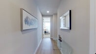 This well-appointed single-floor residence showcases a thoughtfully designed layout that balances comfort and functionality. The entry hallway sets an elegant tone, featuring light hardwood flooring, recessed lighting, a mirrored wall accent, and a sleek glass console table that leads naturally into the living areas.

The living room is a bright, welcoming space lined with multiple large windows that flood the room with natural light and offer outdoor views. A ceiling fan, light hardwood floors, and a generous footprint make it ideal for both relaxing and entertaining.

The kitchen is a standout feature, boasting an expansive quartz-topped island with seating, floor-to-ceiling dark cabinetry, stainless steel appliances, a tile backsplash, and large windows that continue the home's light-filled atmosphere.

The primary bedroom is carpeted and comfortably sized, with a ceiling fan and direct access to an en-suite bathroom featuring a dual-sink vanity with dark cabinetry, large-format dark tile flooring, and a soaking tub. A spacious walk-in closet with built-in shelving completes the suite. A second bedroom offers a similarly serene environment with ample natural light.

A dedicated office nook, in-unit Whirlpool washer and dryer, and consistent neutral-toned finishes throughout contribute to the home's modern, functional character.