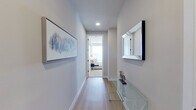This well-appointed single-floor residence showcases a thoughtfully designed layout that balances comfort and functionality. The entry hallway sets an elegant tone, featuring light hardwood flooring, recessed lighting, a mirrored wall accent, and a sleek glass console table that leads naturally into the living areas.

The living room is a bright, welcoming space lined with multiple large windows that flood the room with natural light and offer outdoor views. A ceiling fan, light hardwood floors, and a generous footprint make it ideal for both relaxing and entertaining.

The kitchen is a standout feature, boasting an expansive quartz-topped island with seating, floor-to-ceiling dark cabinetry, stainless steel appliances, a tile backsplash, and large windows that continue the home's light-filled atmosphere.

The primary bedroom is carpeted and comfortably sized, with a ceiling fan and direct access to an en-suite bathroom featuring a dual-sink vanity with dark cabinetry, large-format dark tile flooring, and a soaking tub. A spacious walk-in closet with built-in shelving completes the suite. A second bedroom offers a similarly serene environment with ample natural light.

A dedicated office nook, in-unit Whirlpool washer and dryer, and consistent neutral-toned finishes throughout contribute to the home's modern, functional character.