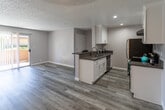 Located at 2011 Arden Ave in San Bernardino, California, this single-story home offers a clean, modern aesthetic with thoughtful updates throughout. The open-concept layout connects the living area and kitchen seamlessly, creating a spacious and functional flow. Light gray laminate wood flooring runs consistently throughout the home, complementing the neutral gray wall tones and crisp white trim.

The kitchen is a standout feature, equipped with white shaker-style cabinetry accented by brushed nickel hardware, dark countertops, and stainless steel appliances including a range, dishwasher, and refrigerator. A peninsula provides additional prep space and enhances the kitchen's open connection to the main living area. Recessed lighting and a ceiling fan add comfort and practicality.

The living area is generously proportioned, bathed in natural light through a large window fitted with vertical blinds, and features a ceiling fan for year-round comfort. A sliding glass door offers access to the exterior. Textured ceilings are present throughout the home.

The bathroom is well-appointed with a white vanity, dark countertop, and a shower-tub combination. The consistent use of laminate flooring extends into this space, tying the home together with a cohesive, updated feel.