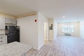 Located at 327 Pine St in Pawtucket, RI, this one-bedroom, one-bathroom unit offers a thoughtfully designed single-floor layout with a clean, modern aesthetic throughout. Light wood-style luxury vinyl flooring flows seamlessly across every room, creating a bright and cohesive feel.

The kitchen is a standout feature, outfitted with shaker-style gray cabinetry, granite-look countertops, a peninsula breakfast bar, and a full suite of black appliances including a range, over-the-range microwave, dishwasher, and refrigerator — ideal for everyday cooking and entertaining.

The open layout connects the kitchen to a dedicated dining area and a spacious living room bathed in natural light from large windows fitted with blinds. A wall-mounted PTAC unit provides climate control in the living area.

The bedroom is a comfortable, well-proportioned room with recessed lighting, a large window with outdoor views, and its own PTAC unit for individualized temperature control. Two closets provide ample storage throughout the unit.

The full bathroom features a tub/shower combo, a gray vanity, and wood-look tile flooring for a polished finish. Additional highlights include a dedicated laundry area and an entrance foyer with utility panel access, completing this functional and well-appointed home.