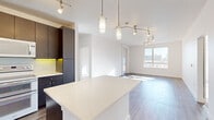 Located at 2201 Lawrence St in Denver's Curtis Park neighborhood, this single-floor residence offers three bedrooms and two bathrooms within a thoughtfully designed layout. The open-concept kitchen is a standout feature, showcasing rich dark cabinetry that reaches the ceiling, crisp white quartz countertops, subway tile backsplash with under-cabinet accent lighting, and white appliances including a double oven range. A large kitchen island provides additional prep space and flows seamlessly into the living area, which is bathed in natural light through expansive floor-to-ceiling windows offering urban Denver skyline views. Hardwood-style flooring runs throughout the main living areas, complemented by track and pendant lighting throughout. The bedrooms are carpeted for comfort, each featuring ceiling fans and generous windows that capture city views. The primary bedroom includes a walk-in closet outfitted with wire shelving systems. The bathrooms are finished with clean tile work, including a full soaking tub with a tiled surround and chrome fixtures. Two hallways and additional closet storage contribute to the unit's functional flow. The overall aesthetic is modern and clean, with a neutral palette of whites and dark wood tones creating a contemporary urban feel.