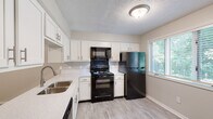 Located at 442 Timber Ridge Dr in Kalamazoo, Michigan, this two-floor residence offers a well-appointed layout with thoughtfully updated finishes throughout. The kitchen is a standout feature, showcasing crisp white cabinetry with brushed nickel hardware, light quartz countertops, and black appliances including an electric range, over-the-range microwave, and refrigerator. Light wood-look flooring runs through the kitchen, complemented by a window that brings in natural light and views of the surrounding greenery. The open dollhouse view reveals a connected main living area that flows naturally between the kitchen and living spaces. Carpeted rooms provide comfort underfoot, including generously sized bedrooms — one featuring a walk-in closet and direct access to an adjacent bathroom. The upper floor offers an open loft-style area with plush carpet, white balustrade railings, and recessed lighting, ideal for a variety of uses. Bathrooms are finished with light wood-look flooring, white vanity cabinetry, quartz countertops, and a tub-shower combination with tile surround. A dedicated laundry closet houses a stacked washer and dryer unit, adding everyday convenience. Neutral gray wall tones and consistent trim work tie the interior together with a clean, modern aesthetic.