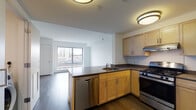 Located at 695 Atlantic St in Stamford, Connecticut, this single-floor residence offers a thoughtfully designed layout with modern finishes and elevated urban views. The open-concept kitchen serves as the heart of the unit, featuring light maple cabinetry, dark countertops, stainless steel appliances including a gas range and dishwasher, and a peninsula with a built-in sink — all set atop rich hardwood flooring. The kitchen flows naturally into the living area, which is bathed in natural light through a large picture window framing views of the Stamford cityscape. The bedrooms continue the clean, minimalist aesthetic — one features the same hardwood flooring and a generously sized window with sweeping city views, while the second bedroom is finished with plush carpeting and its own window overlooking the surrounding neighborhood. The bathroom is finished with classic mosaic tile flooring, a white vanity with a dark countertop, a large mirror, and clean white walls, offering a functional and tidy space. Throughout the residence, crisp white walls, flush-mount lighting, and a neutral palette create a bright and cohesive atmosphere well-suited to urban living in the heart of Stamford.