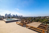 Located in the Echo Park neighborhood of Los Angeles, this rooftop amenity deck at 1011 Everett St offers an exceptional outdoor retreat with panoramic views that stretch across the city. The space is designed to maximize the Southern California lifestyle, presenting unobstructed sightlines of the iconic downtown Los Angeles skyline to the east and the tree-lined hillside neighborhoods and mountain ranges to the west and north.

The rooftop features a tiled spa pool with stainless steel entry rails, ideal for relaxation while taking in the surrounding cityscape. Multiple teak-framed sun loungers with neutral mesh slings are arranged across the sun deck, providing ample space for outdoor lounging and sunbathing. A dedicated seating nook, furnished with teak-framed armchairs and cushioned upholstery alongside a side table, offers a more intimate area for conversation or quiet outdoor relaxation.

The deck surface is finished in smooth, light-toned concrete, and the perimeter is secured with metal railing that preserves the open views while ensuring safety. Architectural elements include modern stucco and corrugated metal facade detailing, lending the space a clean, contemporary aesthetic. The rooftop's elevated position above the neighborhood provides an open-air experience that captures natural light throughout the day, making it a standout communal feature of the property.