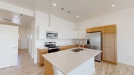 Located at 5602 Shadow Hills Rd in Las Cruces, New Mexico, this single-story, 3-bedroom, 2-bathroom home offers a thoughtfully designed layout with clean, modern finishes. Light-toned wood-look tile flooring runs throughout the home, complementing the crisp white walls and creating a bright, cohesive aesthetic.

The open-concept living, dining, and kitchen area serves as the heart of the home. The kitchen is highlighted by a large central island with a quartz countertop and undermount sink, two-tone cabinetry featuring white upper cabinets and warm natural wood lower cabinets, and a full suite of stainless steel appliances. Soaring ceilings above the kitchen add an impressive sense of volume and openness.

The living area benefits from recessed lighting, multiple windows, and access to an outdoor balcony, inviting natural light and views of the surrounding landscape. A wide hallway connects the bedrooms, each featuring neutral walls, wood-look tile floors, and ample natural light. The spacious primary bedroom includes a generous walk-in closet with built-in shelving. Two full bathrooms are finished with quartz vanity countertops, warm wood cabinetry, rectangular undermount sinks, and brushed nickel fixtures; one features a tub-shower combo. A dedicated laundry room and three closets round out this well-appointed home.