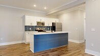 Located at Powell Road in Columbia, SC, this single-floor, 3-bedroom, 2-bathroom residence offers a thoughtfully designed layout finished with contemporary details throughout. The open-concept kitchen and living area serves as the heart of the home, anchored by a standout kitchen island clad in blue shiplap paneling topped with a crisp white countertop and an undermount sink with a matte black faucet. White shaker-style cabinetry lines the walls, complemented by a slate-blue subway tile backsplash and a full suite of stainless steel appliances, including a range, microwave, and refrigerator. Recessed lighting and crown molding add a polished finish to the space. Wood-look plank flooring extends consistently throughout the entire unit, providing warmth and visual continuity. The living area is bright and open, with a glass-paned exterior door allowing natural light to filter in. The primary bedroom offers a generous footprint with a walk-in closet providing ample storage. Additional bedrooms are well-proportioned with neutral walls and the same durable flooring. The bathrooms feature white shaker cabinetry with black hardware and clean countertops, maintaining the cohesive modern aesthetic found throughout the home.