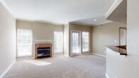 Located at 16650 Huebner Rd in San Antonio, TX, this single-floor residence offers a thoughtfully designed layout with comfortable living spaces throughout. The expansive living room serves as the heart of the home, featuring warm neutral-toned carpeting, crisp crown molding, and a tile-surround fireplace flanked by large windows that invite generous natural light. French doors open directly to an outdoor area, blending indoor and outdoor living seamlessly. The open layout extends into a secondary living or dining area, defined by a curved half-wall that connects to the kitchen. The kitchen is well-equipped with rich dark wood cabinetry, granite countertops, stainless steel appliances including an electric range and over-the-range microwave, and light hardwood flooring that adds warmth to the space. A hallway leads to the private areas of the residence, including a full bathroom finished with tile-accented tub and shower surround, dark granite vanity countertop, dark wood cabinetry, and hardwood flooring. Throughout the residence, neutral warm beige tones, crown molding details, and abundant window coverage create a bright, cohesive, and welcoming atmosphere ideal for comfortable everyday living.