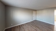 This single-floor unit offers a clean, functional layout with consistent neutral gray tones and warm-toned accents throughout. The kitchen is well-equipped with white cabinetry, a butcher block-style countertop, a double-basin sink, and a full suite of white appliances including a refrigerator, electric range, and dishwasher. Rich wood-look vinyl plank flooring runs through the kitchen and main living areas, providing both durability and visual warmth.

The living area is generously sized, bathed in natural light, and features a textured ceiling and a private entry door. Multiple additional rooms serve as bedrooms, each finished with soft neutral carpet, white blinds, and ample natural light from well-placed windows. One bedroom benefits from dual closets with white bi-fold doors, offering considerable storage capacity. Another room, finished with the same vinyl plank flooring, provides flexibility as a bedroom or multipurpose space.

The full bathroom features a single-sink vanity with a light countertop, a large mirror with overhead lighting, a tiled tub/shower combination, and matching wood-look flooring. Textured ceilings are a consistent design element throughout the unit, complementing the understated, move-in-ready aesthetic of the entire space.