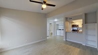 This single-floor residence offers a thoughtfully designed layout that balances open-concept living with practical functionality. The main living area is spacious and airy, featuring vaulted ceilings, a ceiling fan, and light wood-tone flooring that runs throughout the home, creating a warm and cohesive aesthetic. A fireplace anchors one end of the living space, while a window allows natural light to brighten the room. The open layout connects seamlessly to the kitchen and utility areas, making the space feel expansive and easy to navigate. The galley-style kitchen is efficiently designed with ample white cabinetry, stainless steel appliances including an electric range, microwave, and full-size refrigerator, along with a stainless steel sink and generous counter space. The neutral color palette and clean lines give the kitchen a modern, functional appeal. Adjacent to the kitchen, a dedicated laundry area houses a full-size washer and dryer, adding exceptional convenience. The bedroom is generously sized with vaulted ceilings, a ceiling fan, access to natural light through vertical blinds, and a large closet. The bathroom features a full tub-shower combination with a rain-style showerhead and crisp white tile surround. Throughout the home, neutral tones, clean finishes, and practical features come together to create a comfortable and move-in-ready living environment.