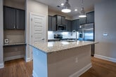 Located at 5060 City Station Way in Collegedale, Tennessee, this single-floor unit offers a well-designed, open layout with consistent hardwood flooring throughout. The kitchen serves as a central focal point, featuring gray shaker-style cabinetry, a white subway tile backsplash, and granite countertops extending across both the perimeter counters and a generous central island. The island is equipped with an undermount sink and overhead pendant lighting with polished chrome fixtures, adding a contemporary touch. A full suite of stainless steel appliances—including a refrigerator, range, microwave, and dishwasher—completes the kitchen. An open pantry with wire shelving provides additional storage.

The living area connects seamlessly to the kitchen and includes recessed lighting and a ceiling fan. French doors lead to an outdoor area, allowing natural light to flow through the space. Bedrooms are fitted with ceiling fans, large windows with blinds, and access to closets with wire shelving systems, including a spacious walk-in closet. The bathroom features a tub-shower combination with chrome fixtures and dark upper cabinetry. A dedicated laundry area includes an in-unit full-size washer and dryer, adding everyday convenience to this thoughtfully appointed space.