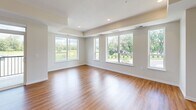 This thoughtfully designed single-floor residence in Delano, Minnesota offers a clean, modern aesthetic defined by warm hardwood-style flooring, crisp white walls, and recessed lighting throughout. The open-concept kitchen and living area serves as the heart of the home, anchored by a generous granite-topped island, white shaker cabinetry, subway tile backsplash, and stainless steel appliances including a gas range. A sliding glass door connects the kitchen directly to an outdoor balcony, flooding the space with natural light and views of the surrounding greenery. The living area features large windows that frame pleasant outdoor scenery, including mature trees and landscaped grounds. Both bedrooms are comfortably sized, featuring plush carpeting, ceiling fans or tray ceiling details, and bright windows with neighborhood views. The primary bathroom is elegantly finished with granite countertops, white shaker vanity cabinetry, a walk-in shower area, and hardwood-style flooring. The secondary bathroom offers a full tub-shower combo with brushed nickel fixtures. Additional conveniences include a hallway with multiple closets, a dedicated laundry room, and a utility room, ensuring practical storage and functionality throughout this well-rounded home.