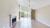 This 2-bedroom, 2-bathroom residence offers a thoughtfully designed single-floor layout with a warm, neutral color palette and wood-style flooring throughout. The living room is a standout feature, boasting soaring vaulted ceilings, a ceiling fan with light fixture, and a classic fireplace with a brick hearth and white mantel. A full-height sliding glass door opens to a balcony, inviting abundant natural light and outdoor views of surrounding greenery. A distinctive arched doorway connects the living area to the hallway, adding an elegant architectural touch. Both bedrooms are comfortably sized, each equipped with ceiling fans and windows that provide natural light and exterior views. The primary bedroom includes a dedicated closet, while the second bedroom also features its own closet for ample storage. The two bathrooms are functionally appointed, with one featuring a tub-shower combination with white tile surround, and the other offering a vanity with a granite-style countertop, undermount sink, white cabinetry, and a large mirror. Textured ceilings are present throughout the residence, adding dimension to the interior. The layout flows efficiently through a central hallway, connecting all rooms with ease.